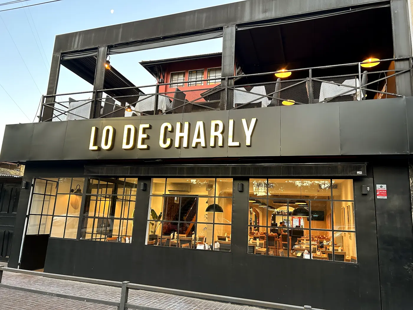 El frente actual de Lo de Charly: fachada negra con letras doradas, ventanales de herrería y terraza en el primer piso